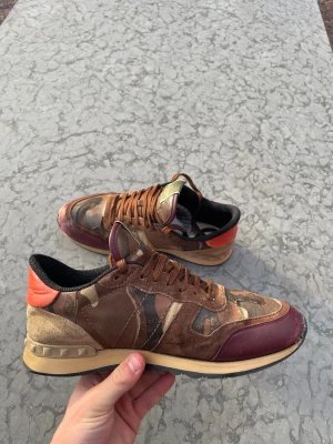 Valentino Garavani Rockrunner sneakers - Säljer ett par Valentino Garavani Rockrunner sneakers med camouflagemönster i brunt, beige och grönt. Finns en liten skada längst fram på skin men det är inget som märks. De är perfekta nu i kylan. Finns tyvärr ingen låda eller tillbehör. Hör av dig vid frågor