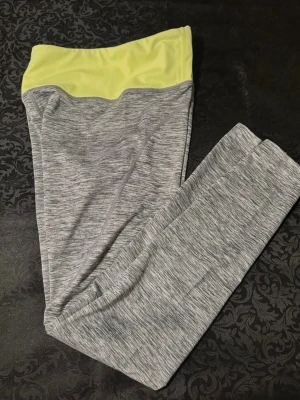 Gråmelerade leggings från Energetics S  - Snygga gråmelerade leggings från Energetics med bred, ljusgul midja och diskret logga framtill. Tillverkade i funktionsmaterial med DryPlus eco för extra komfort vid träning. Tight passform och hög midja för en sportig look.