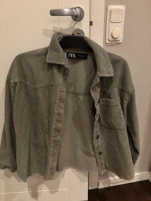 Grön manchester overshirt från Zara - Säljer en chill grön overshirt från Zara i mjuk manchester. Jackan har en klassisk krage, knappstängning framtill och en bröstficka. Perfekt att slänga över en t-shirt för en laidback vibe. Långärmad och med rå kant nedtill för extra edge.