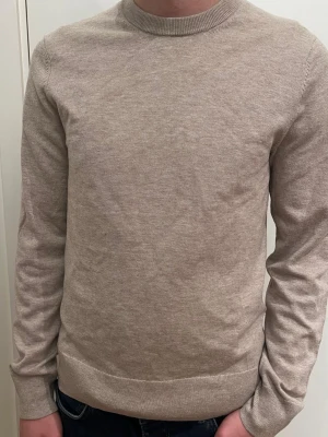 Beige stickad tröja Filippa K XS - Snygg beige merino tröja från Filippa K i storlek XS. Tröjan har rund hals, lång ärm och är tillverkad av merinoull. Enkel och stilren design som funkar till jeans eller chinos. Perfekt för dig som gillar klassiska och mjuka plagg.
