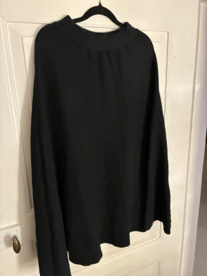 Svart stickad långkjol från Voyelles - En svart långkjol med enkel och stilren design från Voyelles. Kjolen har en lätt utställd form och bred linning upptill. Materialet känns stickat, perfekt för kyligare dagar. Passar dig som gillar klassiska och minimalistiska plagg.