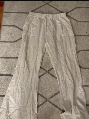 Vita linnebyxor med snörning - Säljer ett par ljusa linnebyxor i vitt med elastisk midja och snörning framtill. Byxorna har raka ben och två fickor fram, vilket gör dem både chill och praktiska. Perfekta för varma dagar när du vill ha en avslappnad vibe.väldigt lågmidjade