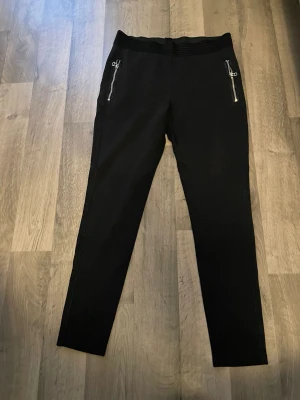 Svarta mjukisbyxor från H&M med dragkedjor - Svarta mjukisbyxor från H&M i storlek L. Byxorna har ribbad midja och två dragkedjeförsedda fickor framtill. Tillverkade i mjukt material med lite stretch för extra komfort. Perfekta för chill dagar eller när du vill ha det bekvämt.