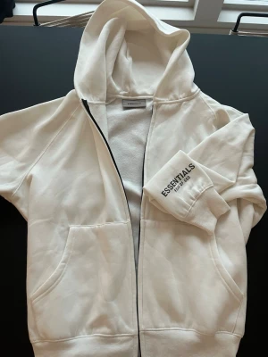 Essentials Hoodie Vit - Vit Essentials zip-up hoodie perfect för de som gillar casual/streetwear 