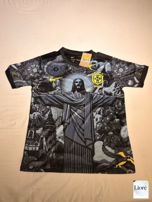 Nike Brasil grafisk t-shirt svart/grå - Snygg svart t-shirt från Nike med Brasil-logga och gult tryck. Framsidan har ett stort grafiskt motiv med Kristusstatyn och detaljer i grått och gult. Korta ärmar med mönster och rund hals. Perfekt för dig som gillar unika fotbollströjor och streetstyle.