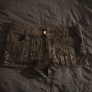 Svarta shorts med paljetter - Säljer ett par svarta shorts med glittriga paljetter framtill. De har låg midja, klassisk knapp och dragkedja samt fickor. Perfekta för dig som vill ha något festligt, säljer pga att de är för små, det är små i storlek