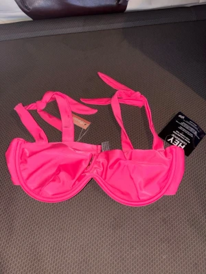 Rosa bikiniöverdel från Nelly - Säljer en snygg rosa bikiniöverdel från Nelly med knyt i nacken och ryggen. Bikinin har bygel och en enkel, stilren design som verkligen poppar med sin starka färg. Perfekt för strandhäng eller poolparty!