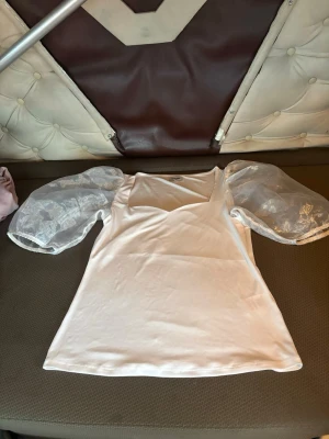Vit topp med puffärmar från Bubbleroom - Säljer en vit topp från Bubbleroom i storlek S. Toppen har transparenta puffärmar i mesh med diskret mönster och en snygg fyrkantig ringning. Kroppen är i mjukt tyg och modellen är normalpassad. Perfekt för dig som vill ha något stilrent men ändå unikt.