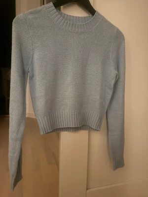 Ljusblå stickad tröja från H&M Divided - Supersöt ljusblå stickad tröja från H&M Divided i storlek XS. Tröjan har rund halsringning, ribbade muddar och är långärmad. Perfekt till lager på lager under höst och vinter. Enkel och clean look som passar till allt.