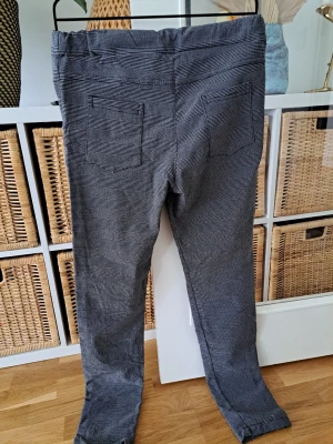 Grå-randiga  byxleggings med snörning - Säljer ett par grå mjukisleggings med tunna svarta ränder och dragsko i midjan. Byxorna har två fickor fram och två bakfickor. Sköna och avslappnade med normal passform, perfekta för chill dagar. Materialet känns mjukt och stretchigt.