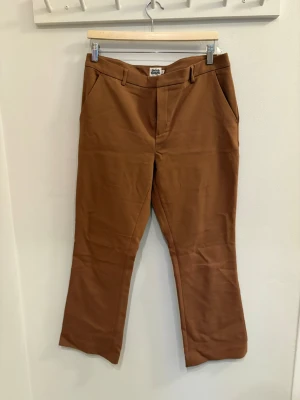 Bruna bootcut kostymbyxor - Snygga bruna kostymbyxor med bootcut-snitt. Byxorna har klassiska fickor fram, hällor för bälte och två dekorativa bakfickor. Tillverkade i ett mjukt bomullsmaterial som känns bekvämt hela dagen.