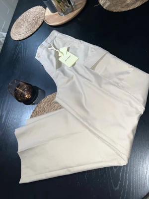 Beiga cargopants från Axel Arigato - Snygga beiga cargopants från Axel Arigato med raka ben och stora fickor på sidorna. Byxorna har bälteshällor och är tillverkade i ett slitstarkt bomullsmaterial. Perfekta för en clean och modern look.