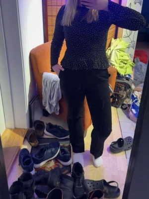 Svarta kostymbyxor med slits - Säljer ett par svarta kostymbyxor med rak passform och liten slits nertill vid benslut. Byxorna har hög midja och klassisk look, perfekta till en snygg outfit. Materialet känns mjukt och stilrent, och de har fickor på sidorna. Obs den går inte att knäppa då knäppet är av! Men de går att fixa lätt!