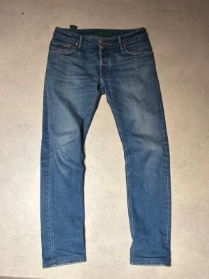 Handpicked blå jeans straight fit - Blå jeans från Handpicked i klassisk straight fit. Jeansen har fem fickor, orangea sömmar och knappgylf. Tillverkade i slitstarkt bomullsmaterial med en snygg tvättad look och subtila slitningar på låren. Storlek 31/32