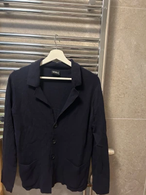Mörkblå kavaj från oscar Jacobsson tunt material - Säljer en mörkblå cardigan jacka från Oscar Jacobson i storlek S. Jackan har klassisk krage, tre knappar framtill och två fickor. Den är stickad och har lång ärm, perfekt för lager-på-lager och en clean look. Nypris ca 2500-3000kr säljs för 1200!! Priset kan diskuteras vid en snabb affär.