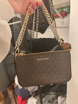 Michael Kors axelväskor BÅDA FÖR PRISET - Två snygga axelväskor från Michael Kors. Ena är brun med MK-mönster och guldfärgad logga, den andra är svart med silverfärgad logga. Båda har en chunky kedja i guld och silver, dragkedja upptill och stilren form. Säljer båda tillsammans för 1000kr. 