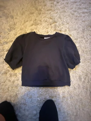 Marinblå  topp med puffärm Gina Tricot - Säljer en marinblå topp från Gina Tricot i storlek 170. Toppen har puffiga korta ärmar och en croppad look. Perfekt till jeans eller kjol. Enkel och stilren design som passar till många olika looks.