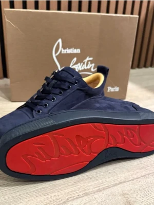 Mörkblå sneakers från Christian Louboutin - Snygga mörkblå sneakers från Christian Louboutin i mocka med klassisk röd sula och diskret logga undertill. Skorna har rund tå, snörning och beige innersula. Perfekta för dig som vill ha en lyxig och stilren sneaker med ikonisk design.