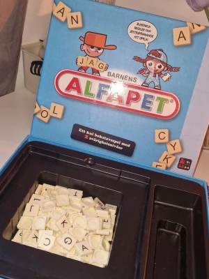 Barn alfapet spel - Spelet har två olika svårighetsnivåer, ett bokstavsspel och ett korsordsspel, på varsin sida av den dubbelsidiga spelplanen. Den enklare varianten kräver inte att man kan stava eller läsa fullt ut, vilket gör det till ett pedagogiskt och lärande spel. Slitage finns på ena sidan av spelplanen- försökt laga med lim, se bild. Brickställen saknas oxå, trots detta går spelet att spela utan problem ändå!