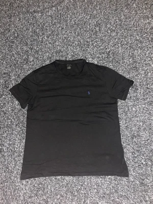 Svart t-shirt från Polo Ralph Lauren - Klassisk svart t-shirt från Polo Ralph Lauren med rund hals och korta ärmar. Diskret blå logga broderad på bröstet. Tillverkad i mjuk bomull som känns skön mot huden. Perfekt basplagg för alla tillfällen. Hör gärna av dig vid intresse / Isak 