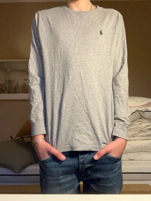 Grå långärmad topp från Polo Ralph Lauren - Säljer en enkel och stilren grå långärmad topp från Polo Ralph Lauren. Toppen har rund halsringning och den klassiska lilla loggan broderad på bröstet. Tillverkad i mjuk bomull som är skön att ha på sig. Perfekt till jeans eller shorts.