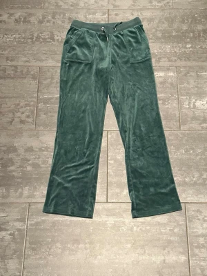 Mörkgröna mjukisbyxor i sammet - !!! Storlek stämmer inte skriv för mått  !!!!!!!Mörkgröna mjukisbyxor i mjuk sammet med bred resårmidja och snörning. Byxorna har raka ben, stora fickor fram och bak med knappdetaljer. Perfekta för chill dagar eller när du vill vara extra bekväm. Använda några få gånger hemma men aldrig ute! Priset kan diskuteras 