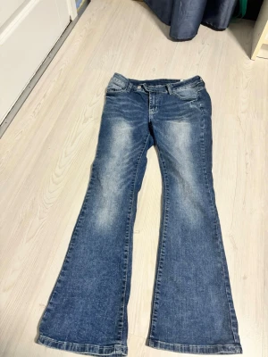 Blå bootcut jeans Shein - Säljer ett par blå bootcut jeans med snygga slitningar och tvättade detaljer. Klassisk fick modell med bälteshällor och knappgylf.