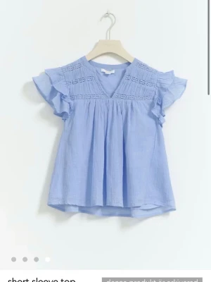 Ljusblå blus med volang från Gina Tricot - Supersöt ljusblå blus från Gina Tricot med v-ringning, volangärmar och broderade detaljer upptill. Stolek 158/164🩵🩵skriv för fler bilder 🥰