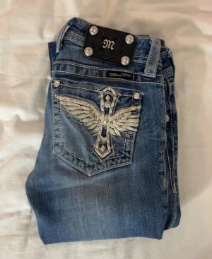 Miss Me Bootcut Lowwaist jeans unika bakfickor - Återpublicerad annons då jeansen tyvärr inte passade mig: Snygga blå Miss Me jeans i bootcut-modell med nitar på bakfickorna. Jeansen har låg midja och detaljerade knappar. Jag är 166 och jeansen är perfekt längd för mig. Som referens har jag xs i toppar. De har ett igensytt hål som du kan se på två av bilderna, det är inget som känns och det är verkligen inget som syns när de sitter på. Skriv till mig om ni undrar något eller om ni vill ha fler bilder 🥰