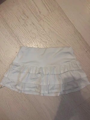 Vit volangkjol från SHEIN XS - Supersöt vit kortkjol från SHEIN i storlek XS. Kjolen har dubbla volanger och är gjord i ett mjukt, stretchigt material. Perfekt för dig som gillar en feminin och sportig vibe. Resår i midjan för skön passform.