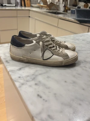 Vita Philippe Model - Säljer ett par vita Philippe Model sneakers med grå mockadetaljer och mörkblå häl. Tvättar dom innan och du får box med!