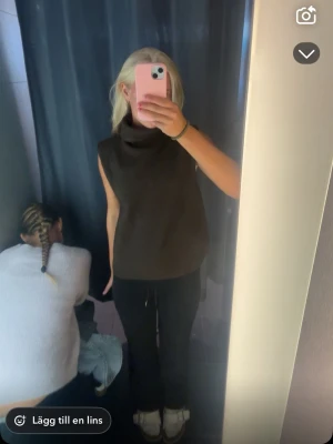 Brun polotopp - Säljer en brun ärmlös polotopp från Amisu i stickat material. Toppen har en hög krage och en rak, lite boxig passform som ger en chill vibe. Perfekt att styla med jeans eller kostymbyxor för en trendig look.