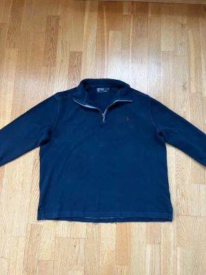 Marinblå half zip från Polo Ralph Lauren - Säljer en marinblå långärmad tröja från Polo Ralph Lauren med klassisk röd logga på bröstet. Tröjan har en snygg half zip-dragkedja och hög krage. Perfekt till höst och vinter, i mjuk bomull som känns skön mot huden.
