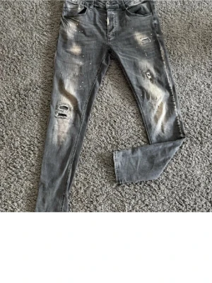 Grå slitna jeans från Alessandro Zavetti - Säljer ett par grå jeans från Alessandro Zavetti med slitningar och distressed detaljer på både fram- och baksida. Jeansen har slim passform, klassisk femficksdesign och coola slitna partier för en edgy look. Bara att höra av sig vid frågor eller liknande! Jeansen är i fint skick!