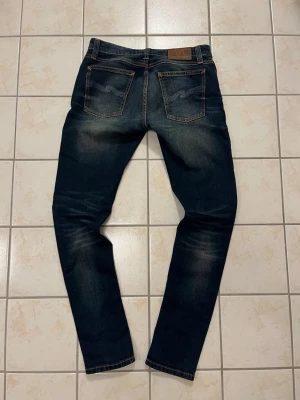 Nudie Jeans blå jeans W29 L32 - Ett par riktigt snygga mörkblå Nudie Jeans med goa slitningar och bra passform.