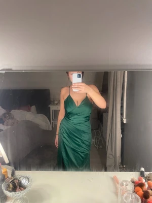 Grön långklänning med snörning - Säljer en smaragdgrön långklänning i glansigt satinliknande material. Klänningen har smala axelband, djup v-ringning, slits framtill och öppen rygg med snygg snörning. Perfekt för bal. Den är perfekt för mig i längden och jag är 164 cm lång. Nypris 1800 kr