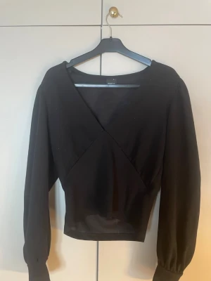 Svart blus topp Gina Tricot S - Säljer en svart omlottopp från Gina Tricot i storlek S. Toppen har lång ärm med bred mudd, v-ringad omlottdesign och croppad passform. Perfekt till jeans eller kjol för en clean look.💘