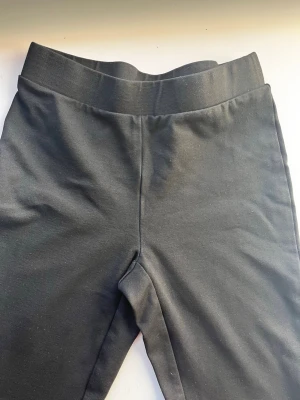 Svarta bootcut byxor från Gina Tricot - Svarta bootcut byxor från Gina Tricot med bred resår i midjan. Byxorna är i stretchigt material och har en enkel, stilren look. Perfekta om du gillar en bekväm men trendig vibe.