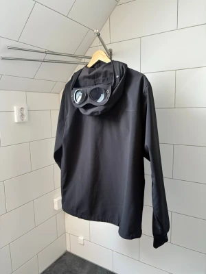C.P. Company Shell-R Google Jacket - Säljer min C.P. Company Shell-R Google Jacket i svart. Köpt på Urban Modern på Väla för lite mer än ett år sedan och sparsamt använd. QR kod, alla tags och kvitto finns kvar. Storlek 50 (L), men skulle säga att den sitter mer som en M. Hör av dig om du har några frågor!