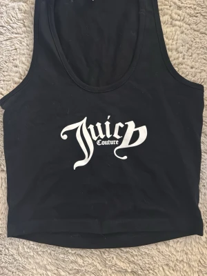 Svart linnetopp från Juicy Couture - Säljer en svart croppad linnetopp från Juicy Couture med stort vitt tryck framtill. Toppen är ärmlös och har en klassisk rund halsringning. Perfekt för dig som gillar en enkel men ändå statement look. Vet däremot inte vad det är för storlek men den passar xs/s.