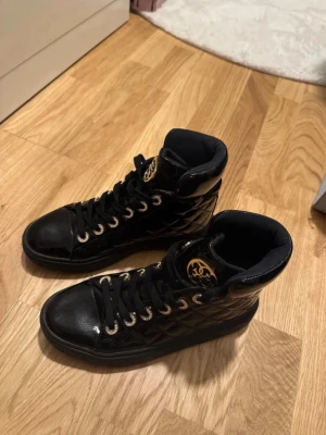 Svarta quiltade sneakers med gulddetaljer - Snygga svarta sneakers från guess. Väldigt bra skick.