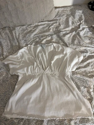 Vit blus med spetsdetaljer White Stag - Säljer en luftig vit blus från White Stag i storlek XL. Blusen har v-ringning, korta ärmar och fina spetsdetaljer längs ringningen och midjan. Materialet är en mix av bomull och polyester med lite struktur, vilket ger en avslappnad känsla.