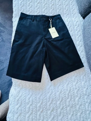 Svarta shorts från Axel Arigato - Stilrena svarta shorts från Axel Arigato med klassisk passform och bälteshällor. Gjorda i ett mjukt bomullstyg som känns skönt mot huden. Perfekta för dig som gillar minimalistisk och clean stil. Passar till allt och är lätta att matcha. Aldrig använt, bara provat. Original etikett sitter kvar.