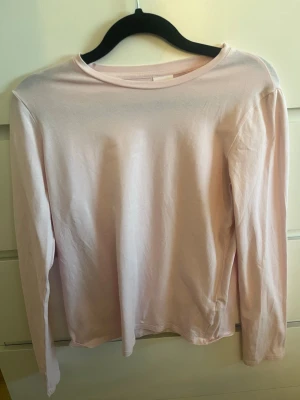 Ljusrosa långärmad topp från Zara - En enkel och stilren ljusrosa långärmad topp från Zara. Tillverkad i mjuk bomull med rund halsringning och rak passform. Perfekt att matcha med jeans eller kjol för en clean look.