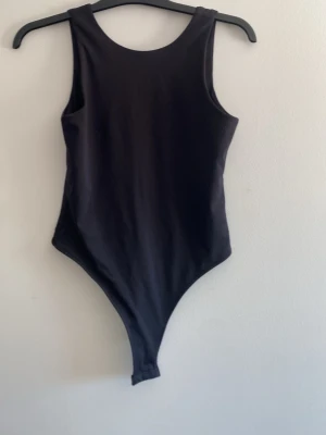 Svart body  - Säljer en svart, enkel och stilren bodysuit med rund halsringning fram och djupare urringning bak. Modellen är ärmlös och har en tight passform som framhäver figuren. Perfekt att styla med jeans eller kjol för en clean look.