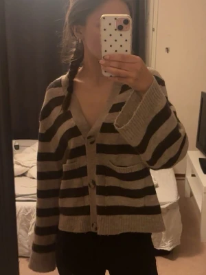 Kofta från Gina tricot  - Säljer en mysig kofta med breda beige och bruna ränder. knappar framtill och två fickor. Den är stickad och har utsvängda armar. 