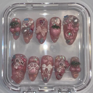 Rosa kawaii press-on naglar med 3D dekorationer - Supergulliga press-on naglar i rosa med glitter och 3D dekorationer som Hello Kitty, rosetter, körsbär, tass och hjärtan. Naglarna har en glansig finish och olika former, dekorerade med pärlor och söta figurer. Perfekt för dig som älskar kawaii och detaljerade naglar.