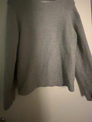 Grå stickad tröja med rund hals - Mysig grå stickad tröja med rund hals och långa ärmar. Tröjan har en enkel och clean look med ribbade muddar vid ärmslut och nederkant. Perfekt för lager på lager under kyliga dagar.