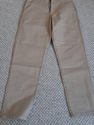 Beige chinos relaxed fit stl 164 - Säljer ett par snygga beige chinos i relaxed fit. Byxorna har klassisk rak passform, bälteshällor och är tillverkade i mjuk bomull. Perfekta för en clean och avslappnad stil. Storlek 164.