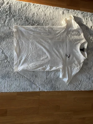 Vit Peanuts t-shirt från H&M XS - Vit t-shirt från H&M i samarbete med Peanuts, regular fit. Framsidan har en liten Snoopy-figur och baksidan har ett stort färgglatt tryck med Snoopy och graffiti-inspirerad text i rött och orange. Klassisk rund hals och korta ärmar. Tillverkad i mjuk bomull.